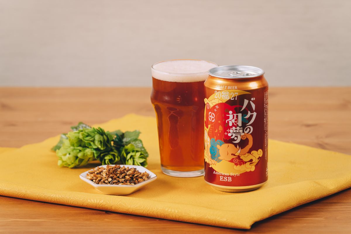 バクの初夢2027とグラスに入ったビール、原料のモルトとホップが並んでいる様子