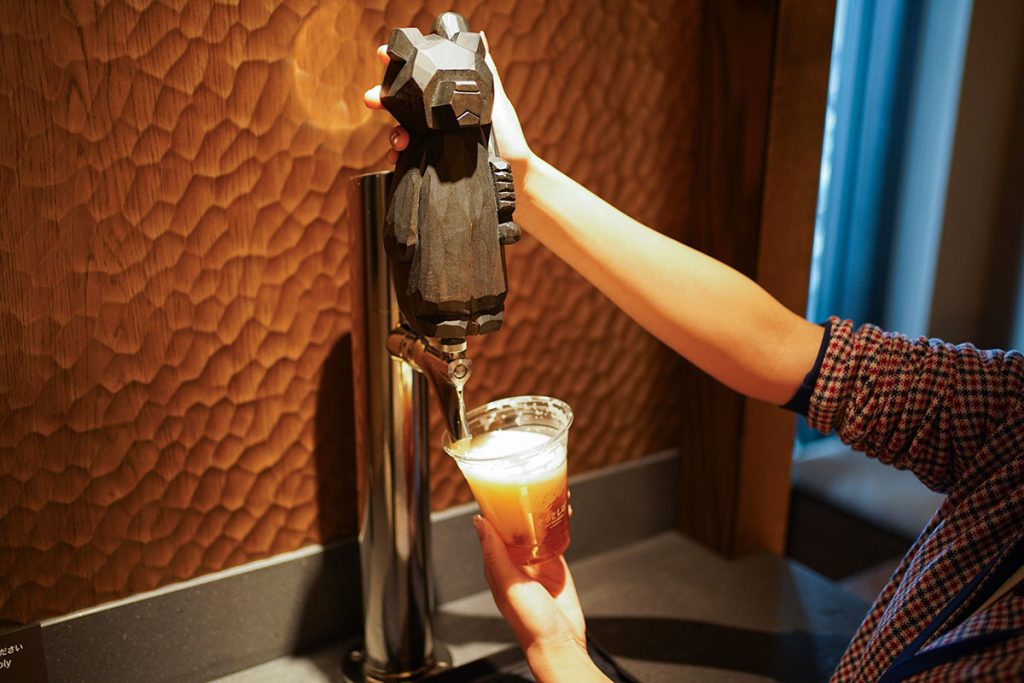 木彫りの熊がヘッドについたビールタップでクラフトビール「そらとしば Play Ball! Ale」を注いでいる様子